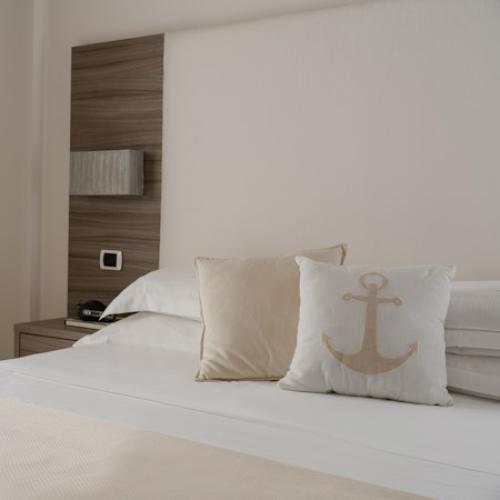 Camera da letto moderna con cuscino decorativo con ancora su letto bianco.