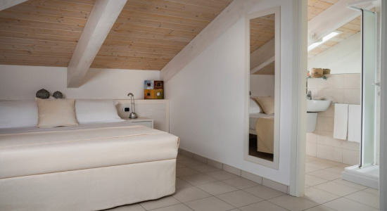 Camera mansardata con letto, bagno privato e soffitto in legno.