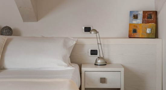 Camera da letto minimalista con soffitto in legno e comodino con lampada.