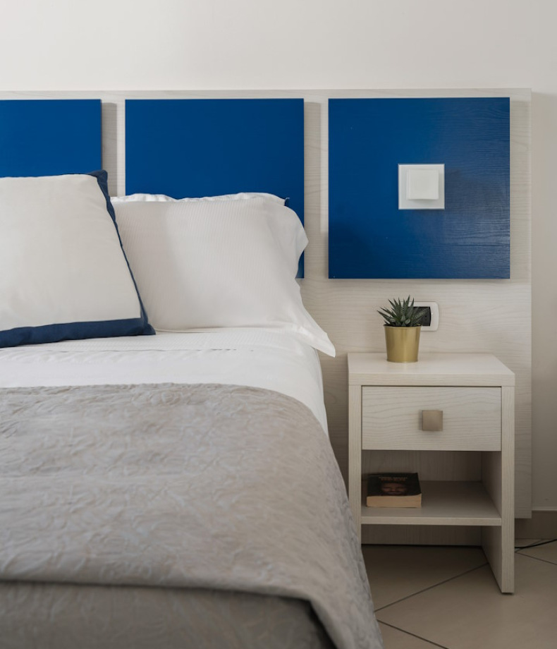 Camera moderna con letto, comodino bianco, pianta e pannelli blu.