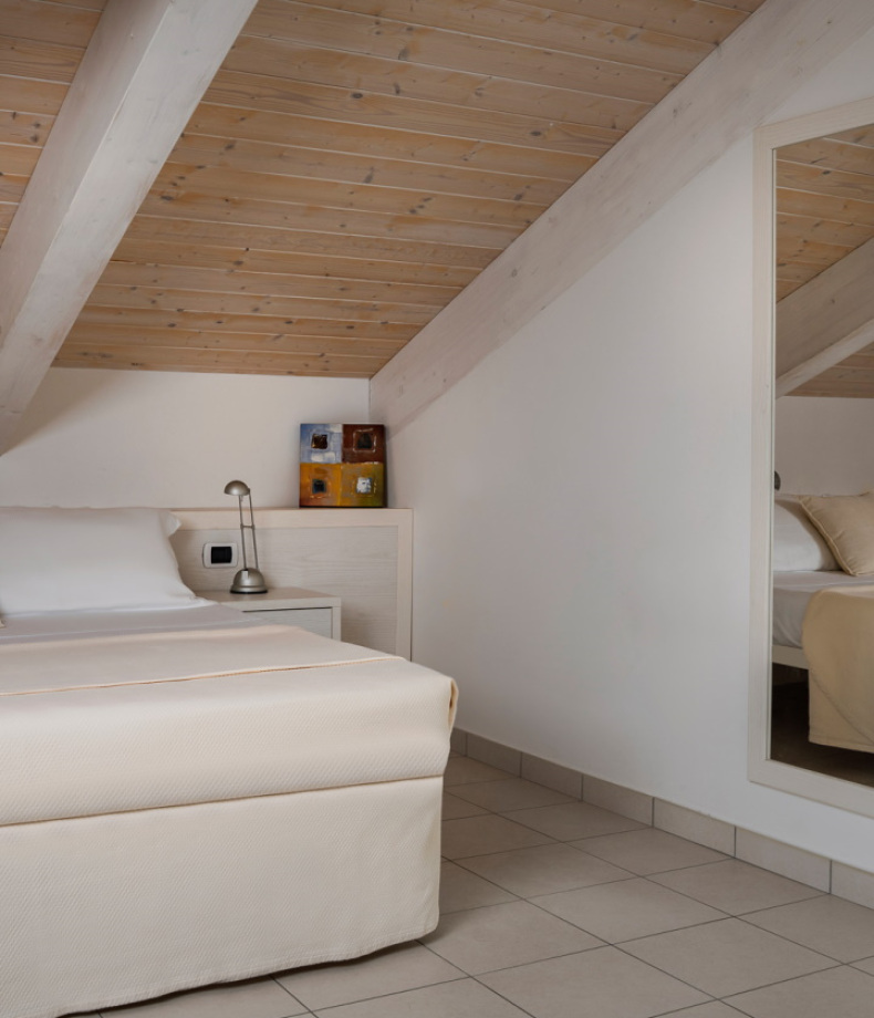 Camera da letto mansardata con letto singolo, lampada da comodino e soffitto in legno.